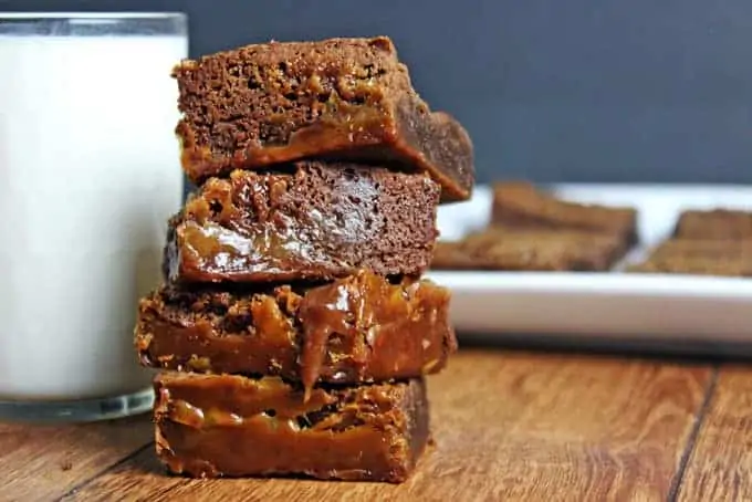 Chocolate caramel brownies stacked on top of each other, with a glass of milk in the background.