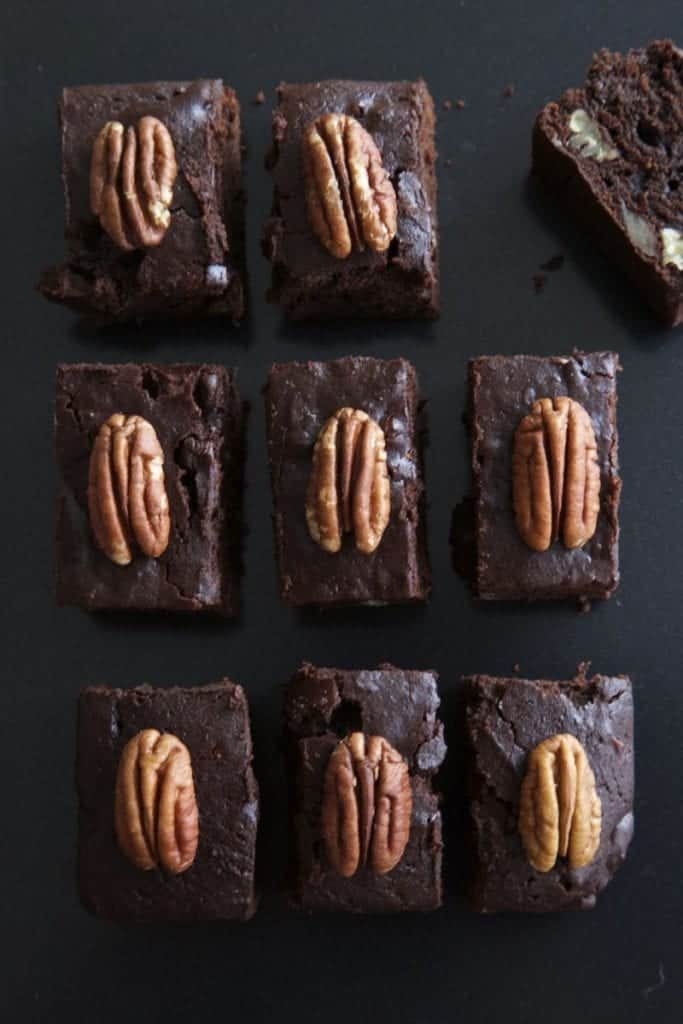 Multiple pecan and pumpkin brownies  on a black surface, with pecan on top.