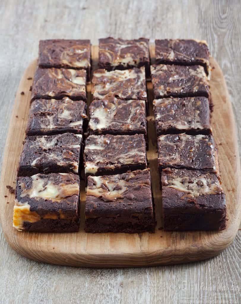 Multiple cheesecake brownies on a wooden board.