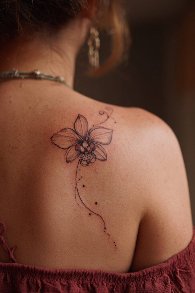 Minimal single orchid bloom tattoo in fine line style.