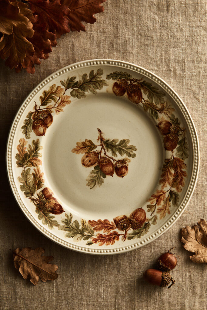 Cream ceramic plate painted with acorns and oak leaves in brown, olive, and ochre around the rim