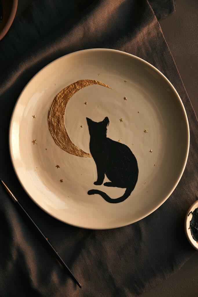 Deep blue ceramic plate painted with a black cat silhouette, crescent moon, and cream stars
