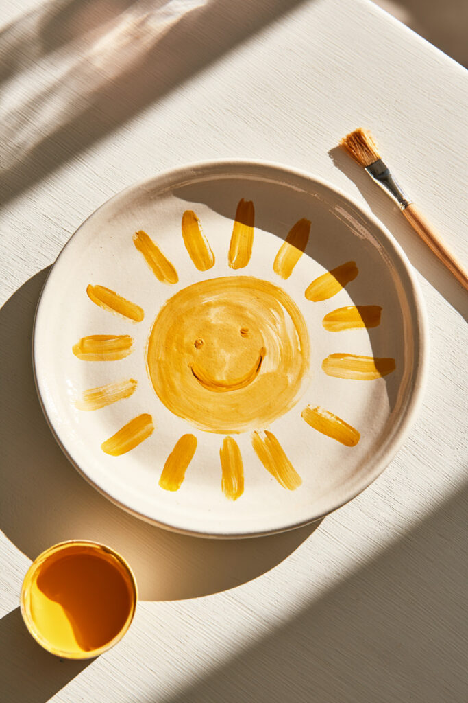 White ceramic plate painted with a smiling yellow sun in the center