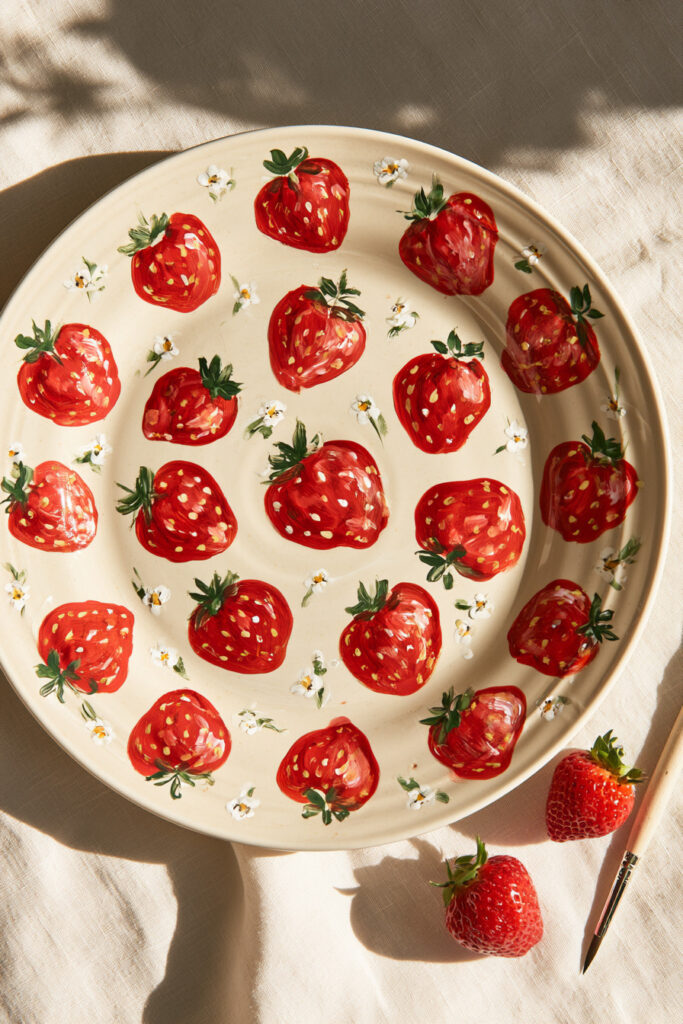 White ceramic plate painted with red strawberries and green tops